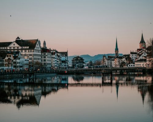 Wide panorama of Zurich Old Town reflecting in the calm Limmat River with historic landmarks like Grossmünster and Fraumünster, a top photo stop for city sightseeing tours.
