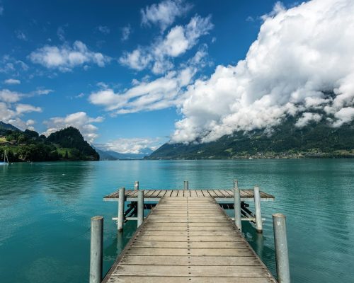 Scenic view of Lake Brienz in Switzerland with turquoise water, wooden dock, lush green hills, and dramatic cloud formations — featured on Zurich Private Tours.