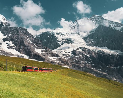 Scenic view of the Jungfraujoch train in Switzerland passing green alpine meadows with the Eiger and Mönch mountains in the background — featured on Zurich Private Tours.