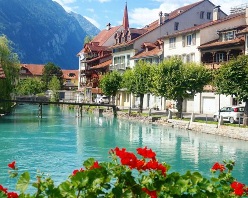 Private tour photo of Interlaken, Switzerland, showing the city center with traditional houses, the Aare River, mountain backdrop, and colorful alpine flowers, as part of Zurich Private Tours' exclusive Bernese Oberland excursions.